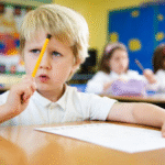 A young boy thinking at his desk, symbolizing challenges of perverted education in modern classrooms