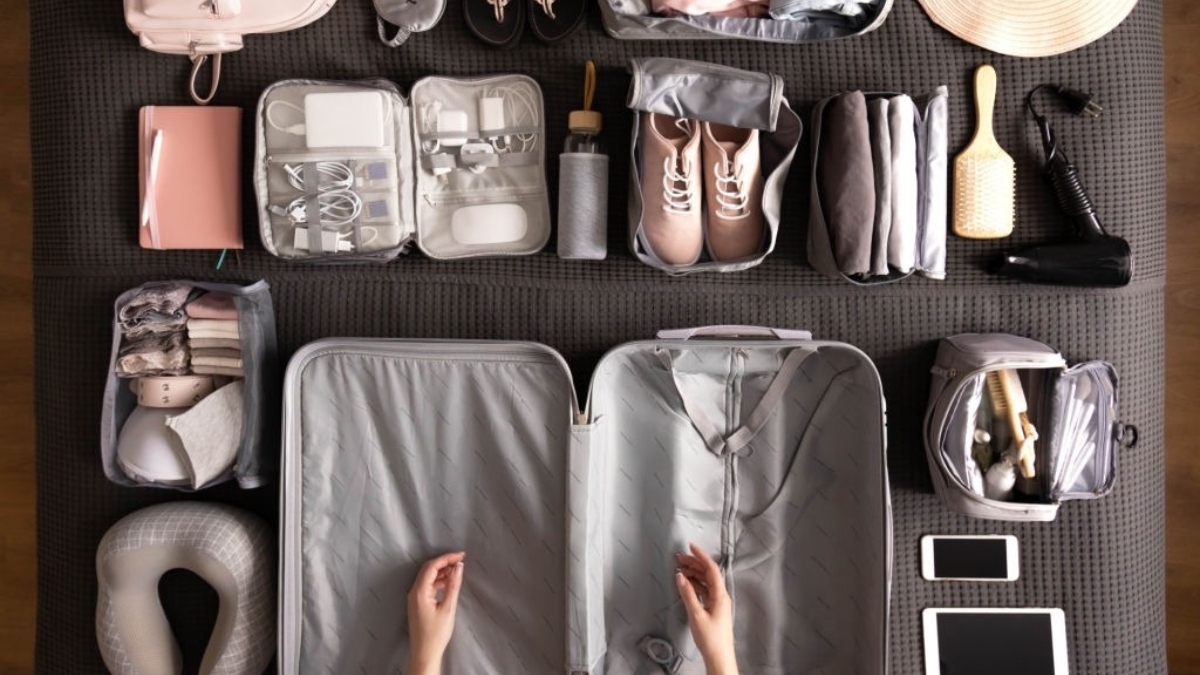 Top-down view of a meticulously organized travel setup featuring a suitcase, packing cubes, and travel essentials in muted grey and pink tones. This image highlights efficient packing travel hacks for a stress-free journey