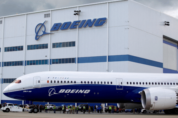 A white and blue Boeing Factory Tour 787-10 Dreamliner sits outside a large white hangar with a blue stripe and the Boeing logo