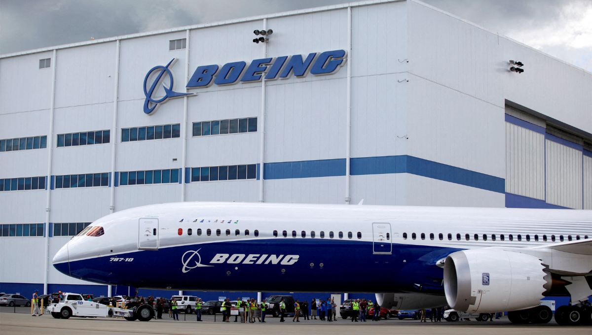 A white and blue Boeing Factory Tour 787-10 Dreamliner sits outside a large white hangar with a blue stripe and the Boeing logo