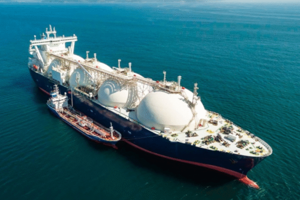 Energy Transport Logistics: Challenges and Innovations An aerial shot captures the intricate process of energy transport logistics, showing a massive LNG carrier with its distinctive spherical tanks being refueled by a smaller tanker on the open ocean