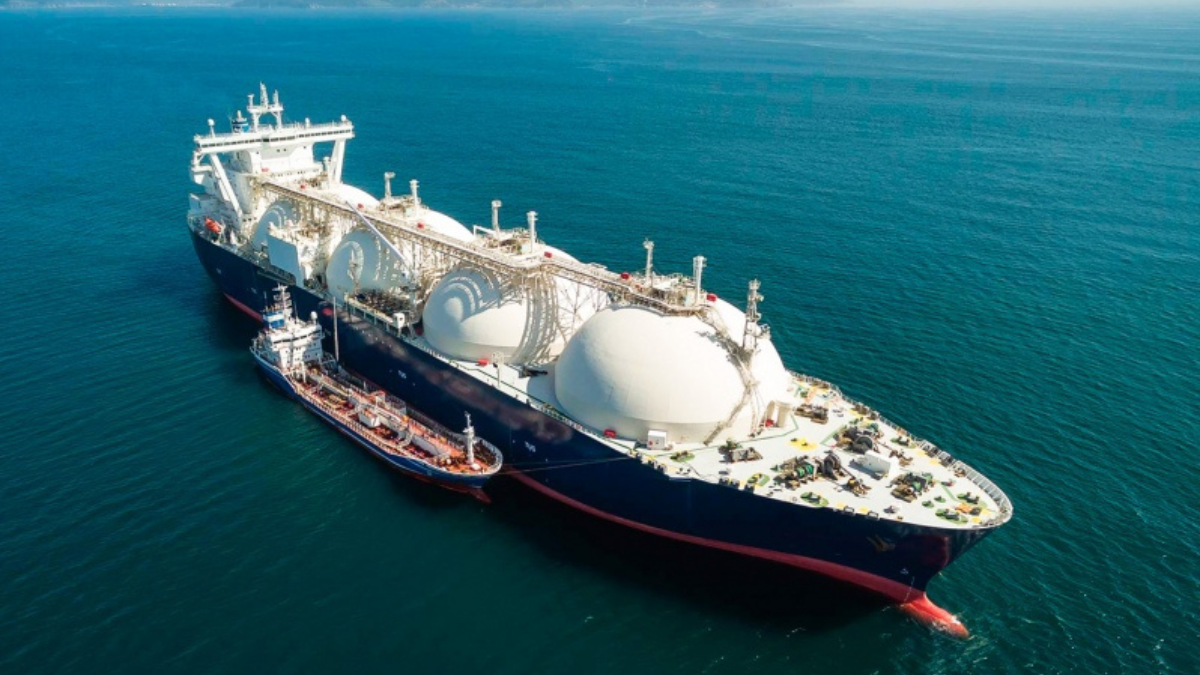 An aerial shot captures the intricate process of energy transport logistics, showing a massive LNG carrier with its distinctive spherical tanks being refueled by a smaller tanker on the open ocean