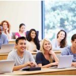 A diverse group of college students in a lecture hall. Some students are using laptops. The students are smiling. Financial Aid Guides for Students