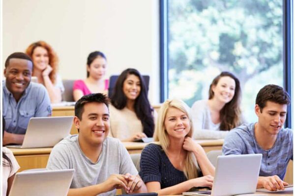 A diverse group of college students in a lecture hall. Some students are using laptops. The students are smiling. Financial Aid Guides for Students