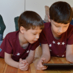 Two young boys on a floor viewing a tablet, symbolizing the potential negative impact of short content on children's minds.